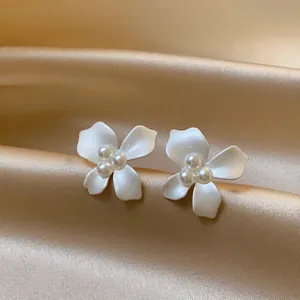 Detailed view of elegant white matte flower earrings with pearl centers on satin