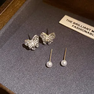 Detailed macro view of delicate silver butterfly and pearl stud earrings on a gray tray
