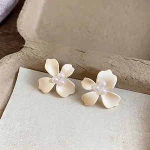 Detailed close-up of cream enamel flower stud earrings with elegant pearl centers