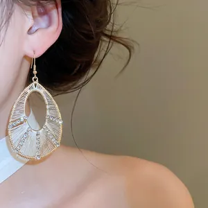 Primo piano di orecchini a goccia dorati con filo intrecciato e strass lucenti sulla modella