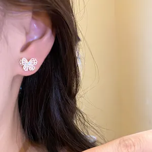 Close-up of a delicate silver butterfly stud earring with sparkling stones on a model's ear.