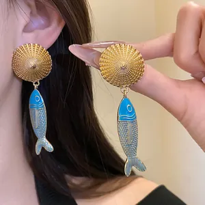 Close-up of vintage gold earrings with blue enamel fish pendants and textured studs