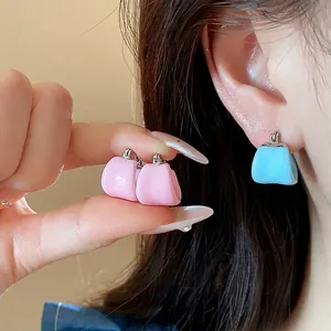 Minimalist U-shaped enamel hoop earrings in pink and blue, worn by model for size reference