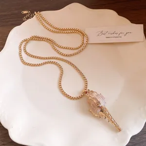 Détail d'un collier avec pendentif en coquillage doré minimaliste sur une assiette blanche