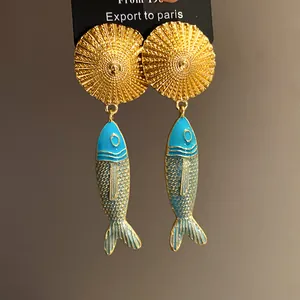 Macro view of vintage enamel fish pendant earrings featuring elegant golden sunburst studs.