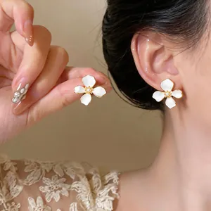 Close-up of white enamel flower earring with pearl center and gold-plated edges for women