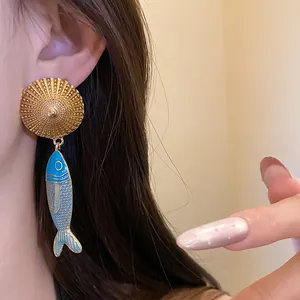 Detailed view of vintage-inspired enamel fish drop earrings with golden textured studs