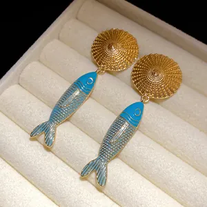 Close-up detail of vintage-style gold and blue enamel fish pendant earrings in a jewelry box.