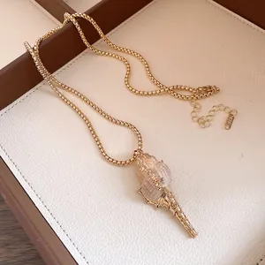 Détail macro d'un pendentif en coquillage naturel avec bordure dorée et chaîne box.