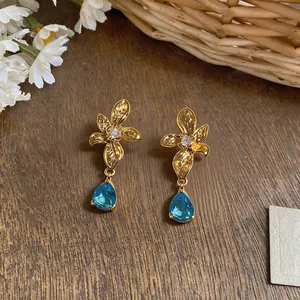 Detailed view of elegant gold floral earrings featuring shimmering blue teardrop gemstones