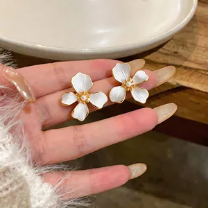 Close-up of elegant 18k gold-plated pearl flower earrings with white enamel finish.