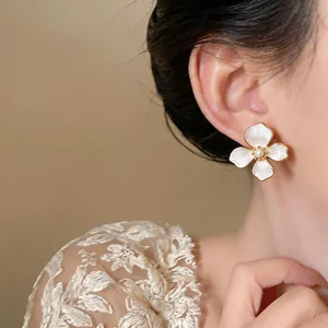Elegant 18k gold plated white flower earrings with central pearl detail on an Asian model's ear