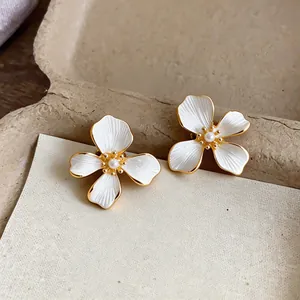 Close-up of elegant flower earrings with white enamel petals, gold plating and pearl center.