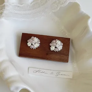 Elegant floral stud earrings featuring pearls and zircons on a dark wooden display block.