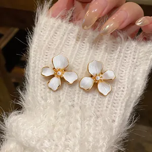 Detailed view of white enamel flower earrings with pearl centers and gold plating.