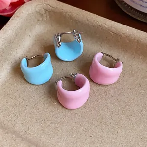 Close-up of pastel pink and blue enamel U-shaped hoop earrings on a beige tray