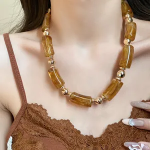 Dettaglio di collana vintage con acrilico ambrato e perle dorate indossata da modella.