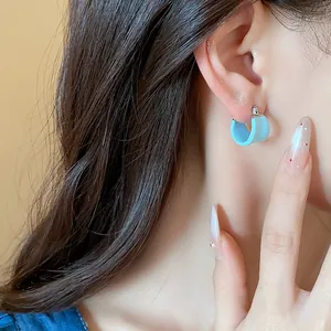 Macro detail shot showing light blue enamel U-shaped hoop earring on a model ear