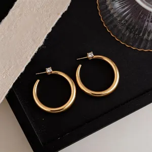 Dettaglio di eleganti orecchini a cerchio placcati oro con piccoli accenti di zirconi quadrati.