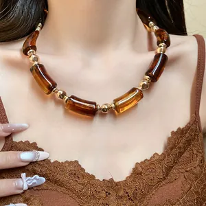 Dettaglio di una collana vintage in acrilico ambra e perle dorate su una modella.