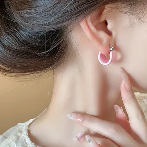 Detailed close-up of pink oil drop U-shaped hoop earrings on ear with chic nails