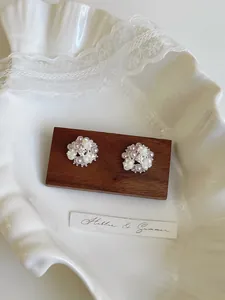 Detailed view of elegant floral stud earrings with pearls and zircons on a wooden block.