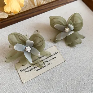 Macro view of unique green mesh flower stud earrings featuring elegant pearl centers