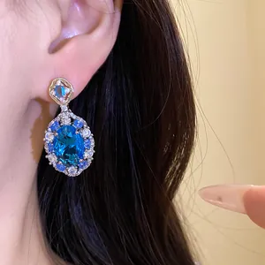Primo piano di elegante orecchino di zircone blu ovale con un alone di pietre brillanti