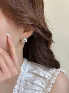 Close-up of elegant flower stud earrings with pearls and zircons worn on model's ear
