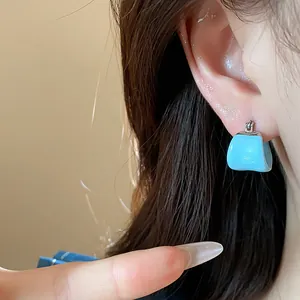 Close-up detail of a minimalist light blue drip oil U-shaped hoop earring on ear