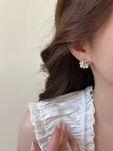 Detail view of elegant zircon and pearl flower stud earrings worn on a model's ear.