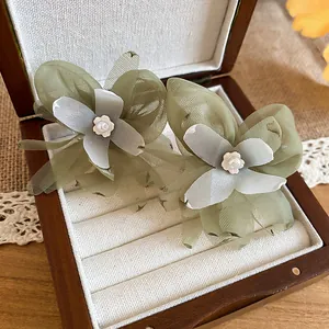 Close-up detail of fresh green mesh flower earrings with white pearl centers in a wooden box