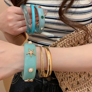 Close-up of resin starfish and pearl bracelet with gold metal bangle stack.