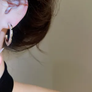 Close-up view of a minimalist silver geometric wavy hoop earring worn on a person's ear
