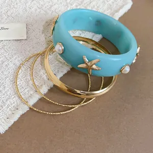 Close-up view of a light blue resin bangle set with gold starfish and pearl details for beach style