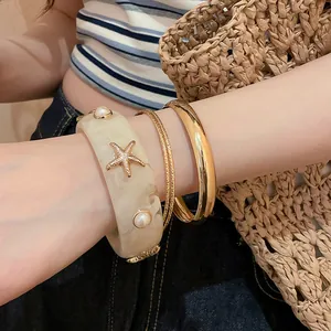 Macro view of cream resin starfish bracelet and shiny gold bangles set for women