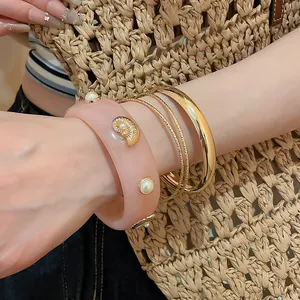 Close-up of pink resin bangle with pearls and gold metal bracelet set on a model's wrist