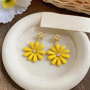 Close-up detail of yellow glass daisy earrings on a white textured plate for summer
