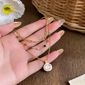 Detailed close-up of a gold-plated multilayer necklace with colored beads and a white enamel pendant.