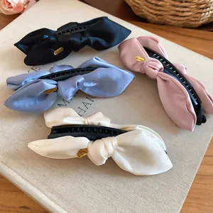 Vier Satin-Schleifen-Bananenspangen in verschiedenen Farben auf einem beigen Buch
