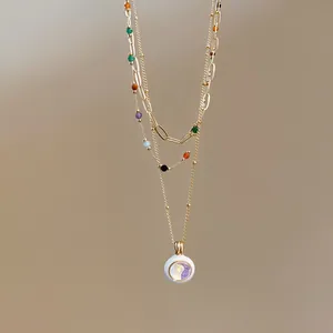 Close-up of a layered gold necklace with colorful stones and white enamel pendant.
