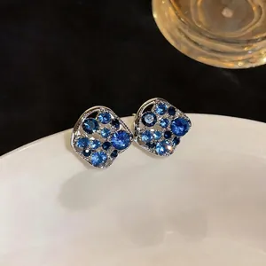 Elegant hollow square stud earrings with blue rhinestones on a white ceramic plate