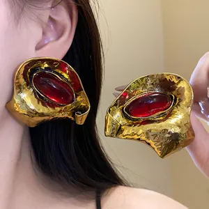 Dettaglio di grandi orecchini vintage dorati con importanti pietre ovali in resina rossa
