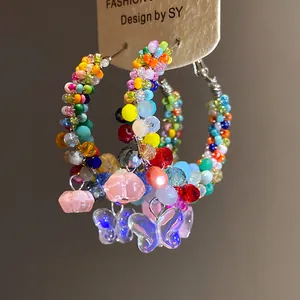 Close-up of colorful crystal beaded hoop earrings with iridescent butterfly charms.