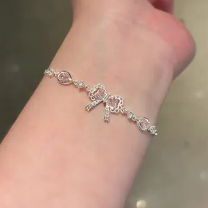 Detail of a delicate silver bracelet featuring a pink zircon bow and heart-shaped stones.