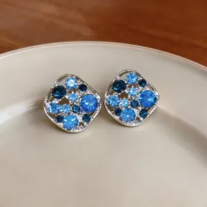 Detailed close-up of square openwork stud earrings with sparkling blue crystals