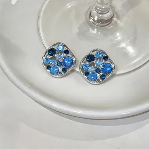 Detail view of silver-toned hollow square stud earrings with blue rhinestone inlay.