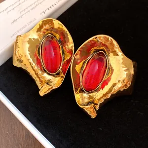 Dettaglio di orecchini vintage in metallo dorato martellato con resina ovale rossa.