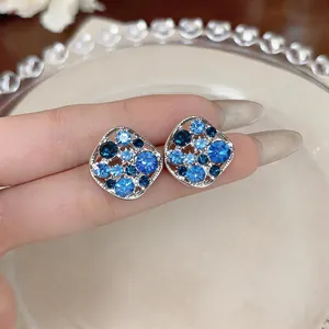 Close-up of blue rhinestone hollow square stud earrings held on fingers for scale