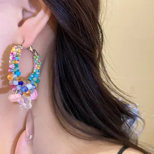 Close-up of colorful crystal beaded hoop earrings with butterfly charms on a model.